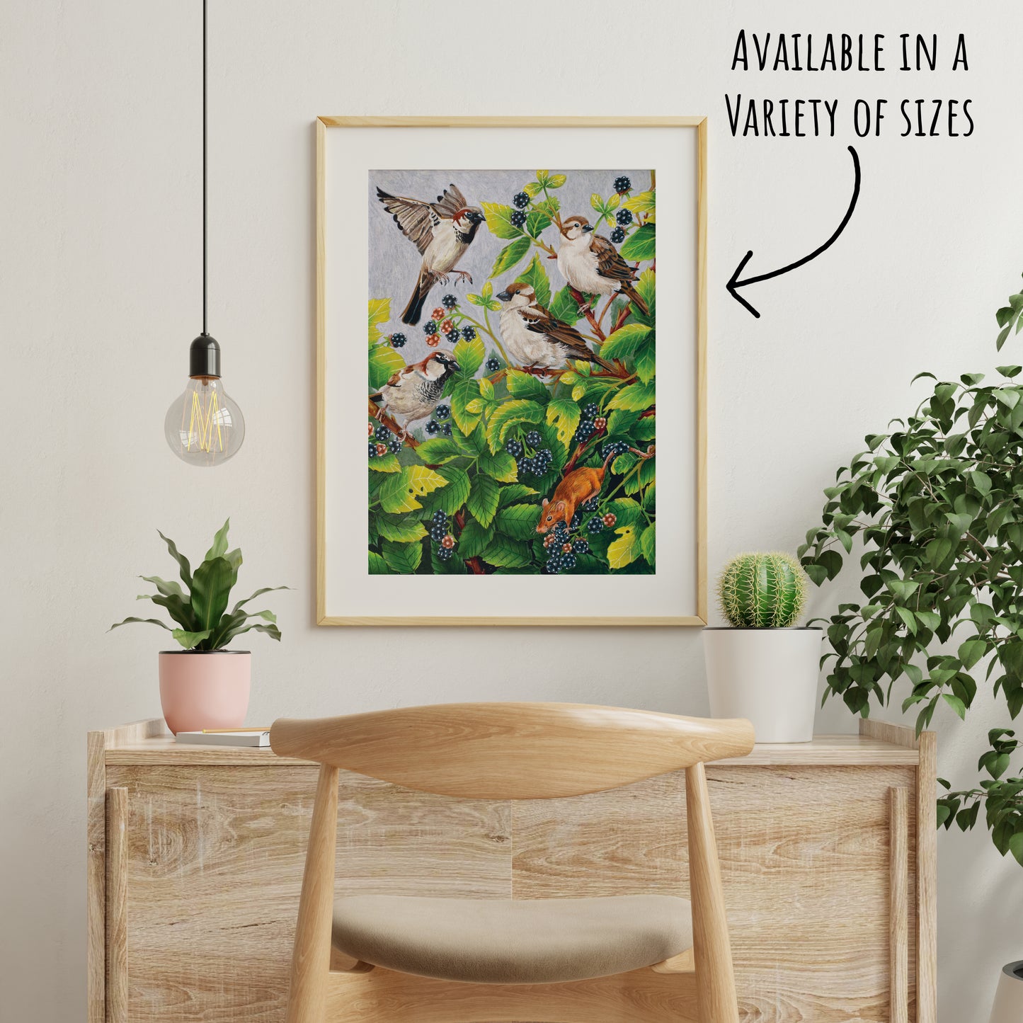 Framed artwork of birds on a branch with leaves and berries, displayed on a wall above a wooden cabinet.