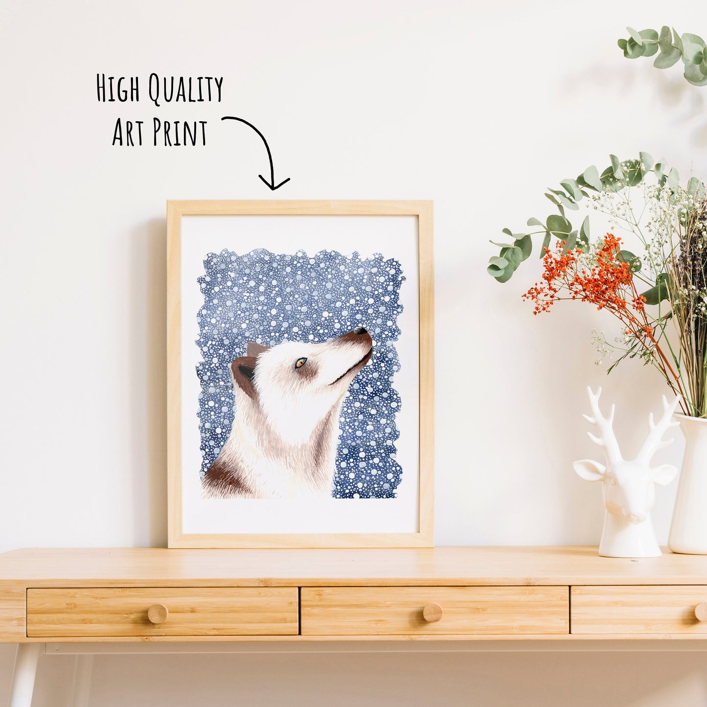 An Arctic fox art print in a light wood frame on a table top with a vase of dried foliage. (frame not included with purchase)