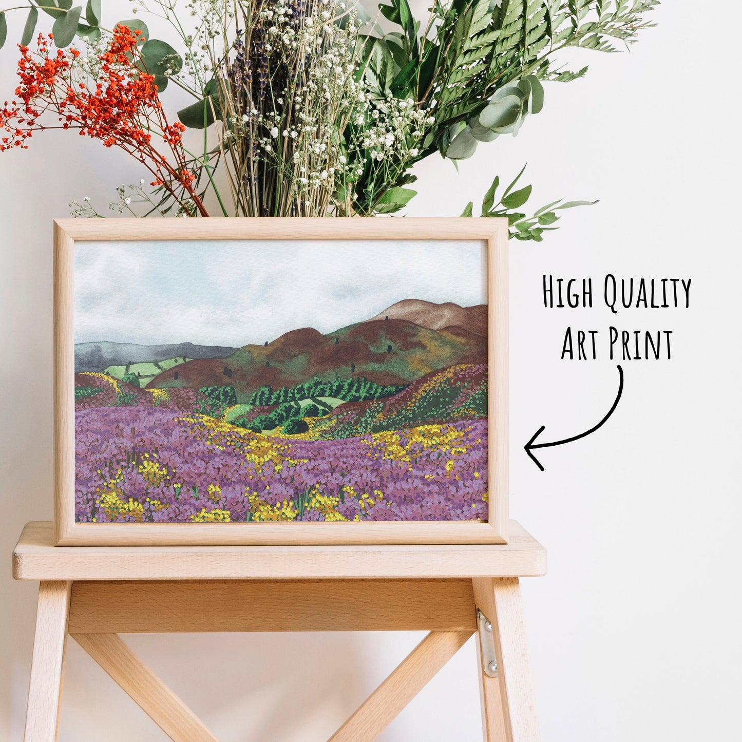 Heather Hills Art Print in a light wooden frame on a coffee table with dried foliage behind.
