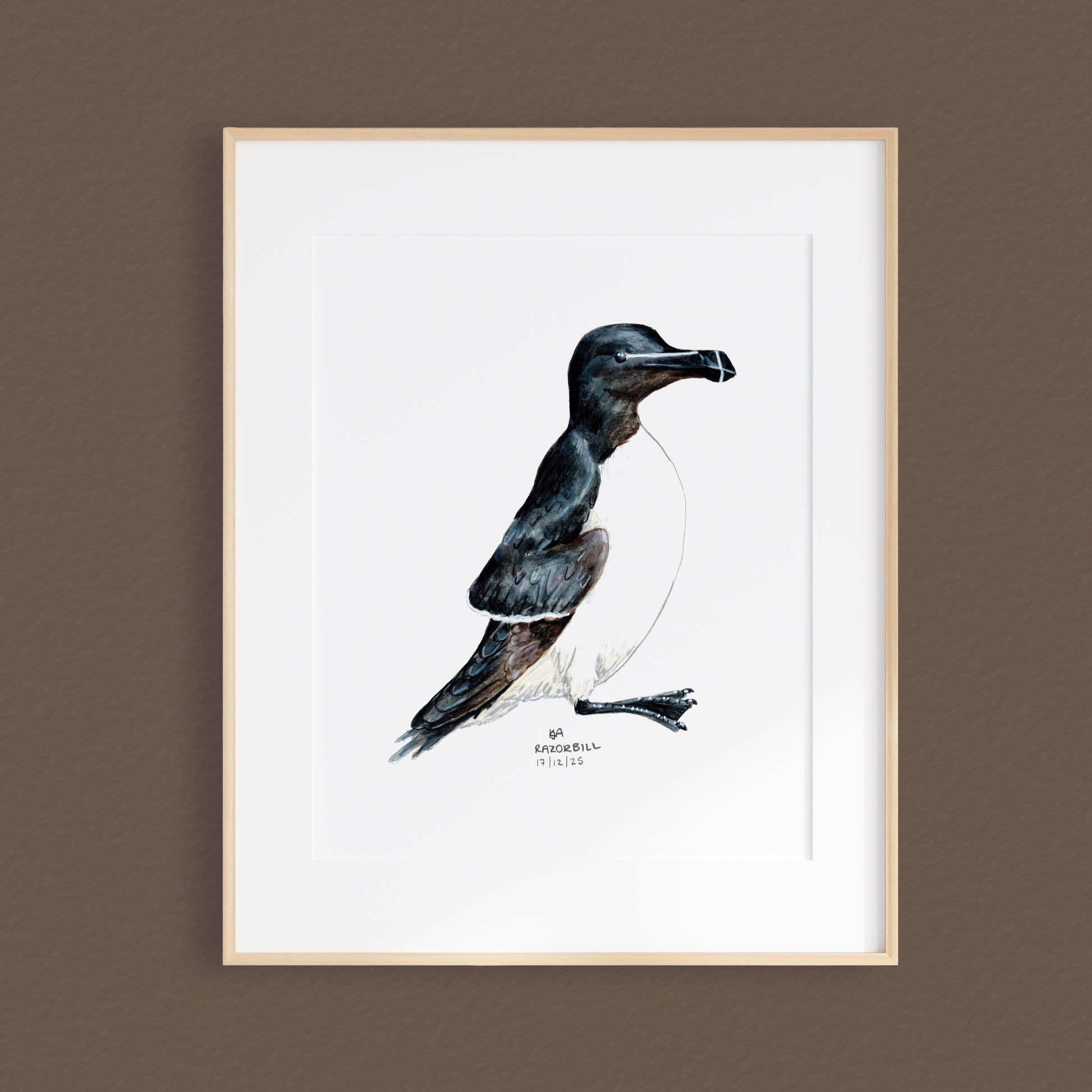 A framed mixed media original painting of a Razorbill bird featuring a light wood frame on white, displayed against a textured brown wall.