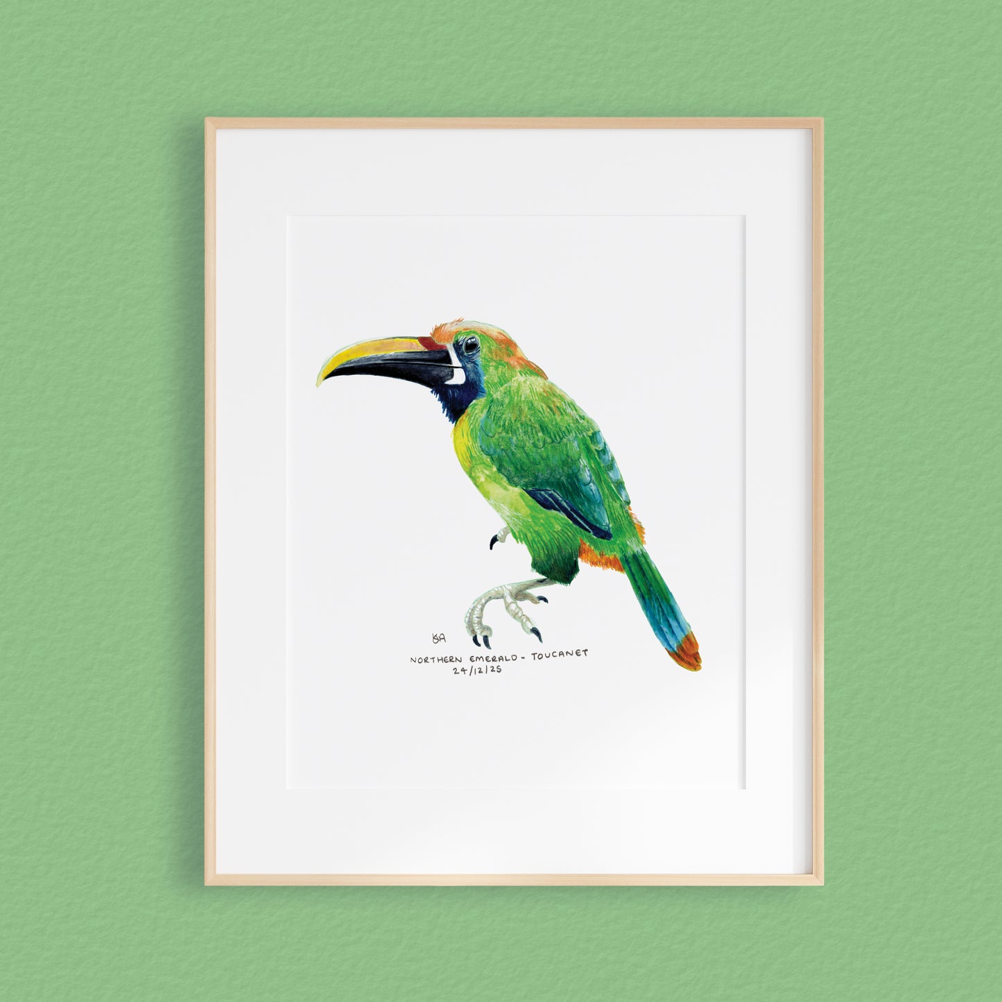 A framed mixed media original painting of a emerald green toucanet bird featuring a light wood frame on white, displayed against a textured green wall.