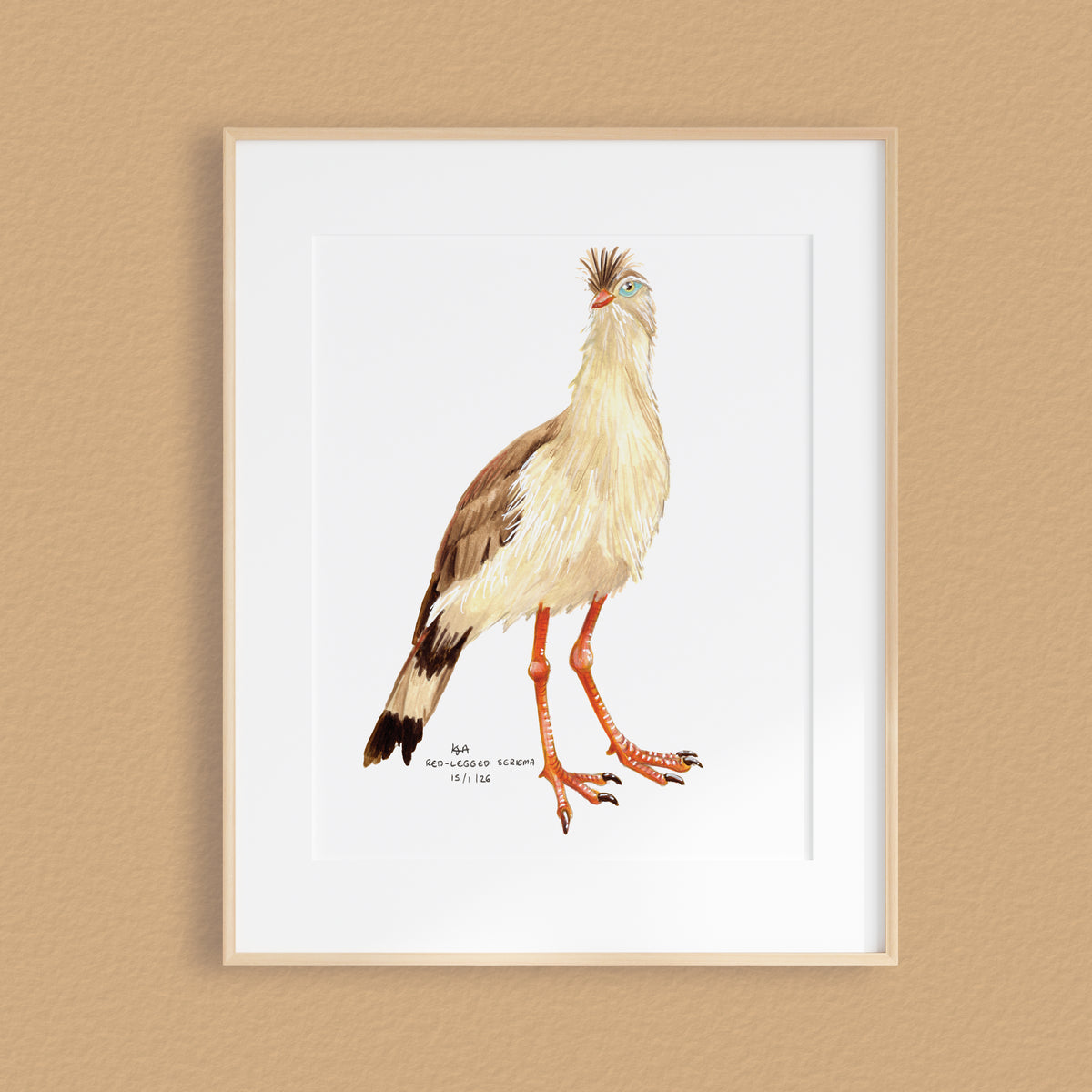 A framed artwork featuring a detailed watercolor illustration of a crested bird with brown, cream, and black feathers, orange legs, and a small black-and-white inscription near the bottom, displayed on a warm beige wall.