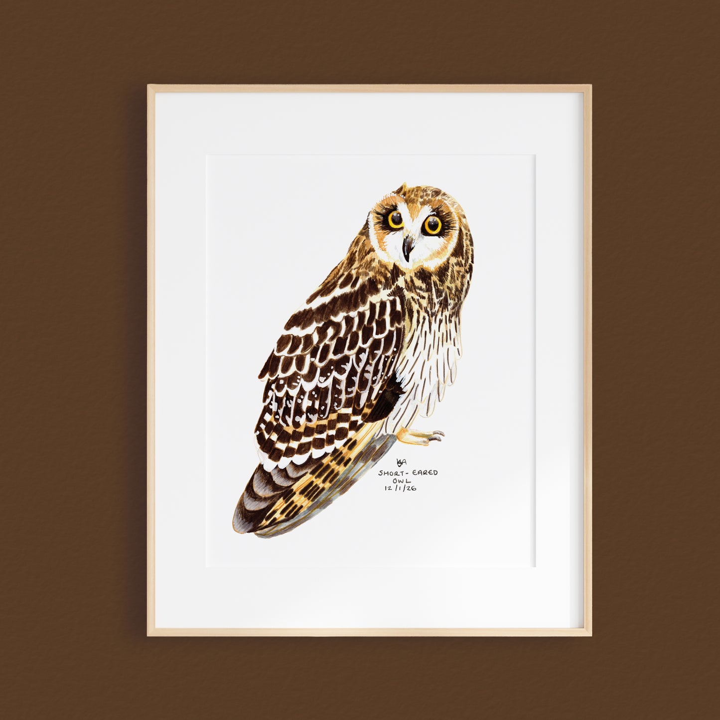 A framed mixed media original painting of a short eared owl, featuring a light wood frame and white, displayed against a textured brown wall.