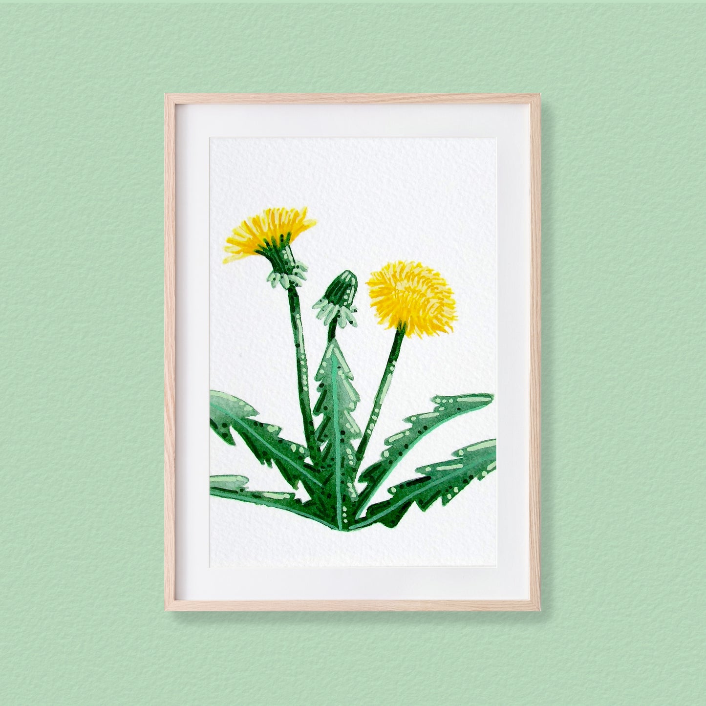 A framed mixed media original painting of a Dandelion featuring a light wood frame on white, displayed against a textured pale mint green wall.