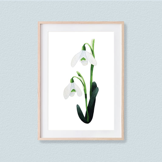 A framed mixed media original painting of a snowdrop flower featuring a light wood frame on white background, displayed against a textured light pale blue wall.