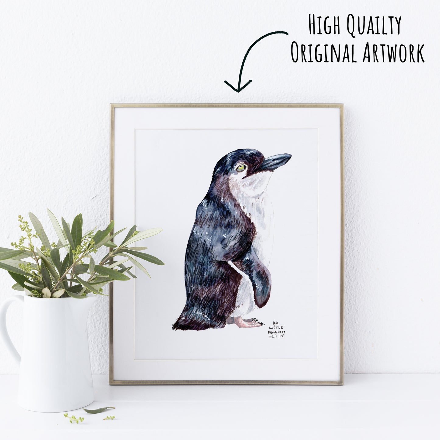Framed artwork of a Little Penguin on a white wall with a plant to the left.