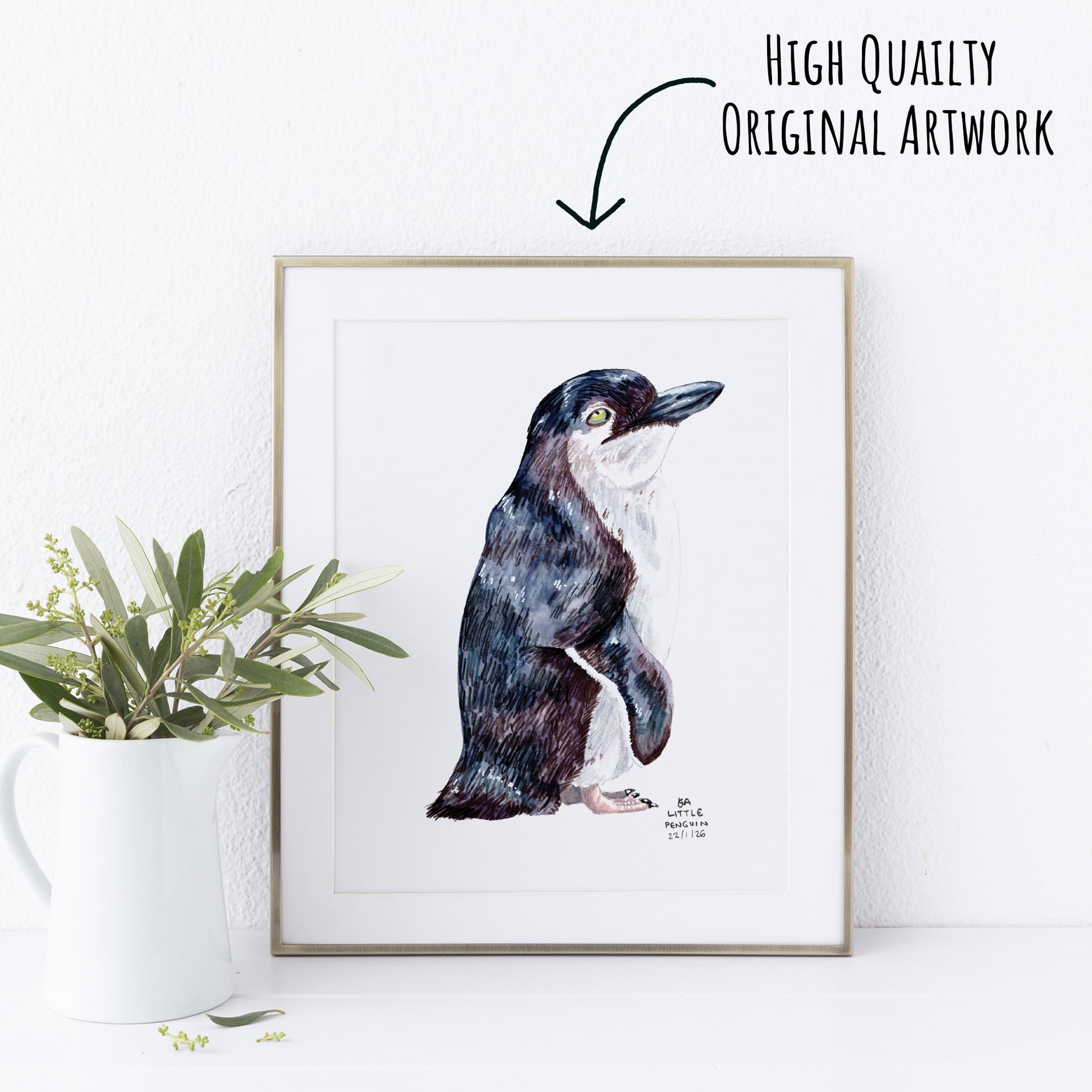 Framed artwork of a Little Penguin on a white wall with a plant to the left.
