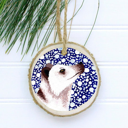 A hand-painted wooden Christmas ornament featuring a white Arctic fox on a dark blue snowy background, with natural pine wood and a jute twine string for hanging.