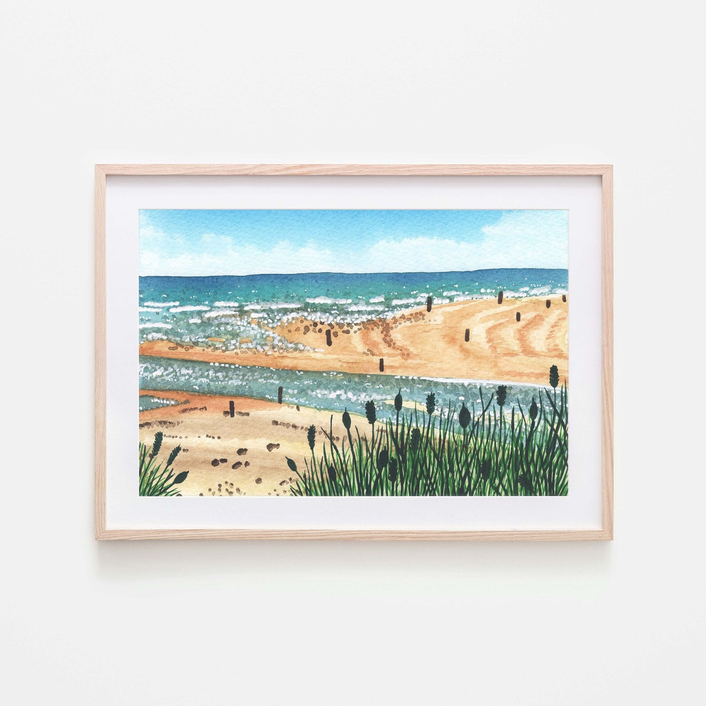 A watercolor art print depicting Beadnell bay with the beach and ocean in the background, framed in a light wooden frame.