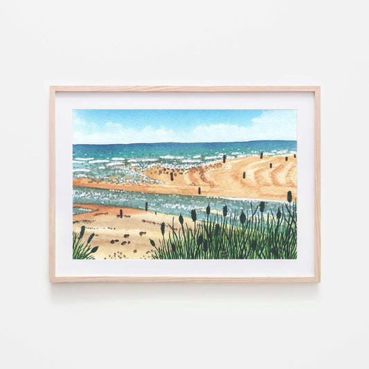 A watercolor art print depicting Beadnell bay with the beach and ocean in the background, framed in a light wooden frame.