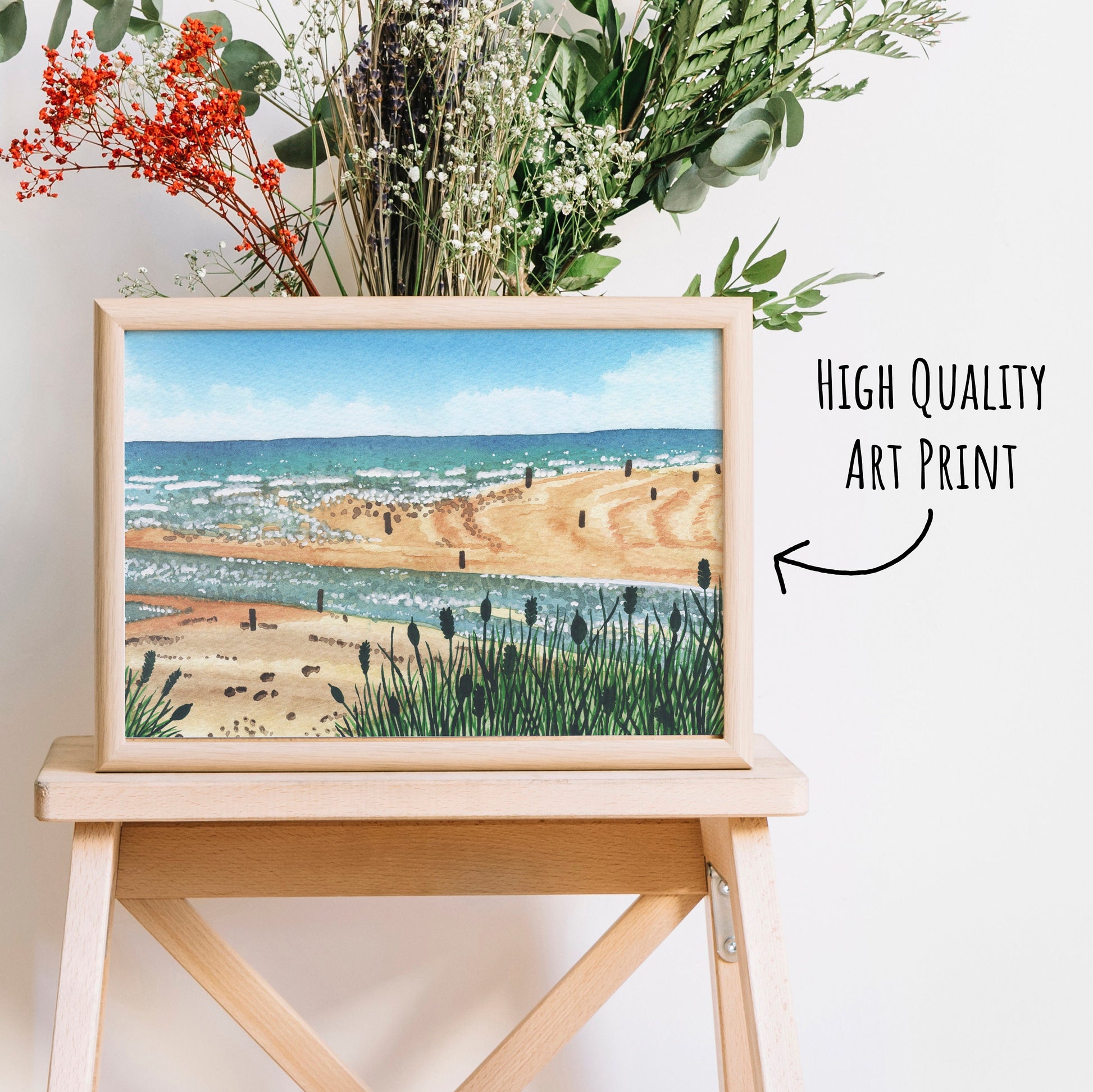 Beadnell Bay Art Print show in  light wooden frame place on a side table with dried foliage behind. (frame not included in purchase)