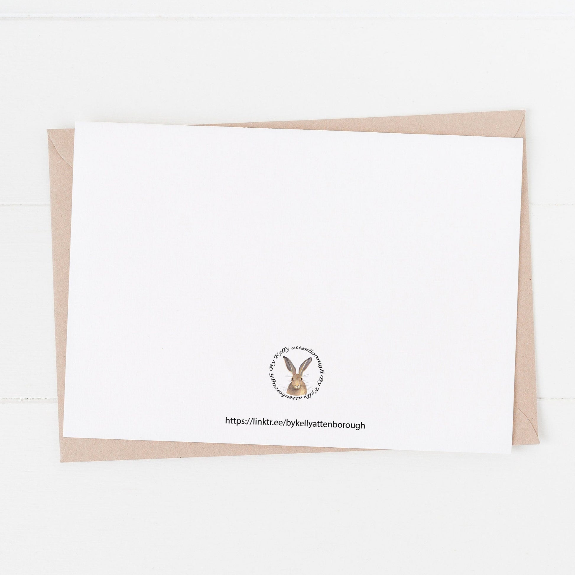 Beadnell Bay beach Birthday Card showing the back with the brand logo laying on a kraft envelope on a white surface.