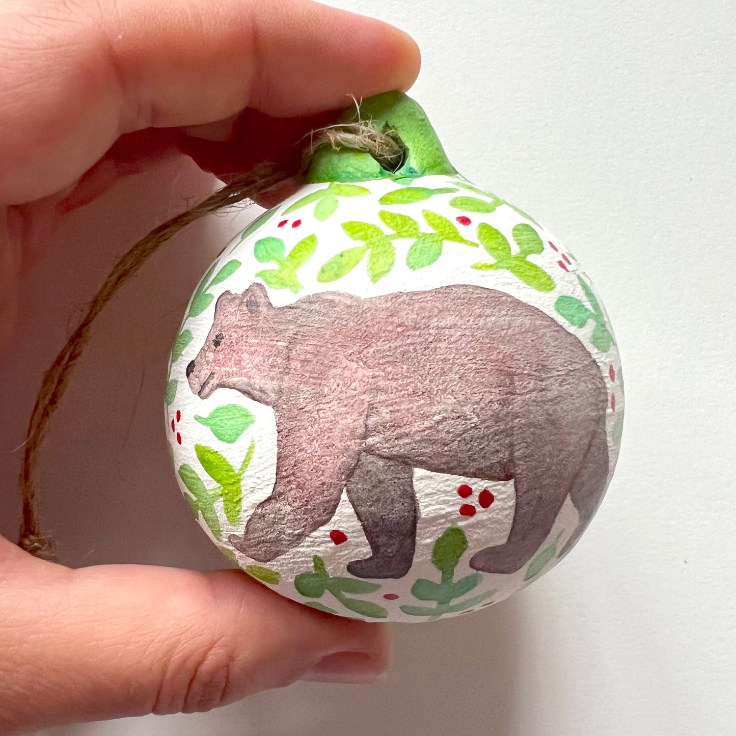 A collection of hand-painted ceramic Christmas baubles with various woodland animal designs including a fox, bear, deer, robin, rabbit, and squirrel, surrounded by green blue leaves and red berries.