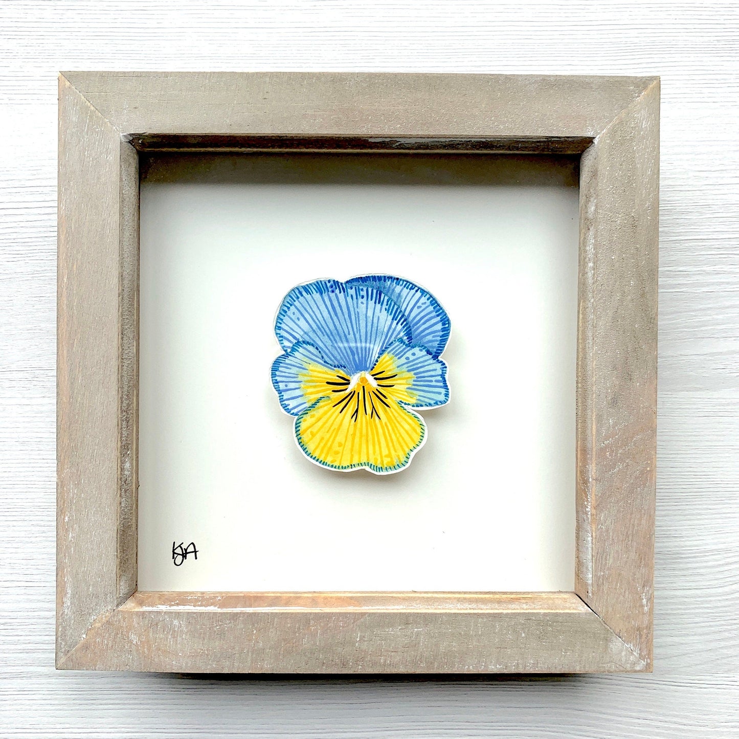 A hand-painted watercolor artwork of a blue and yellow pansy flower in a rustic washed effect frame.