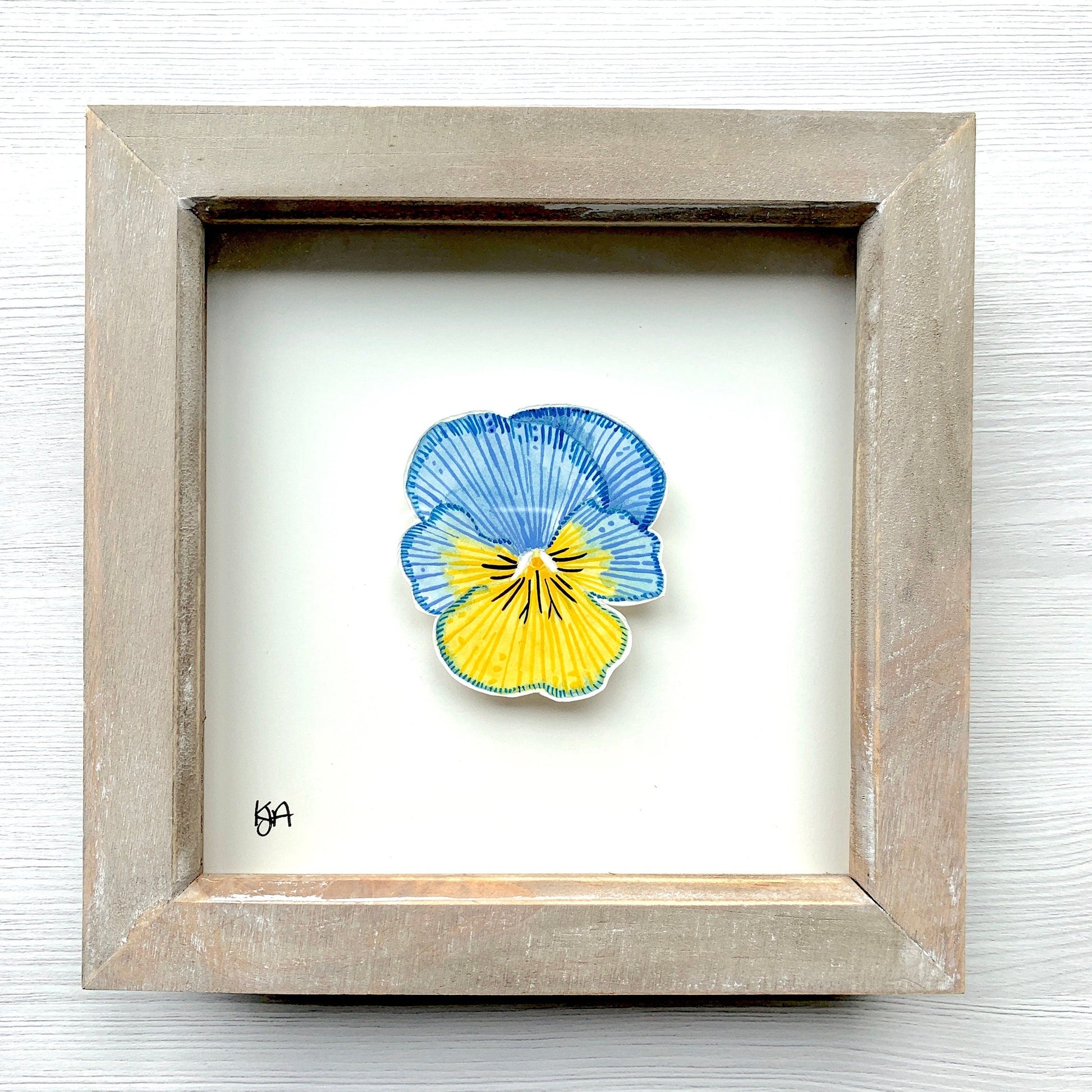 A hand-painted watercolor artwork of a blue and yellow pansy flower in a rustic washed effect frame.