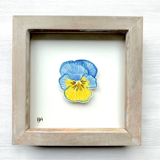 A hand-painted watercolor artwork of a blue and yellow pansy flower in a rustic washed effect frame.