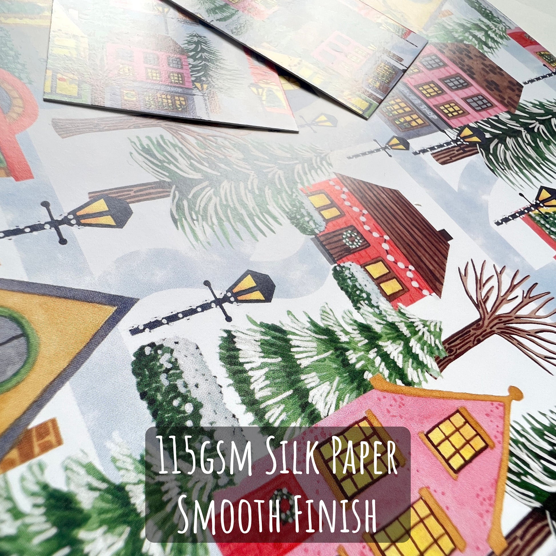 Christmas Village Wrapping Paper close up showing the details of the illustration and the paper stock. with the text 115gsm silk paper smooth finish. 