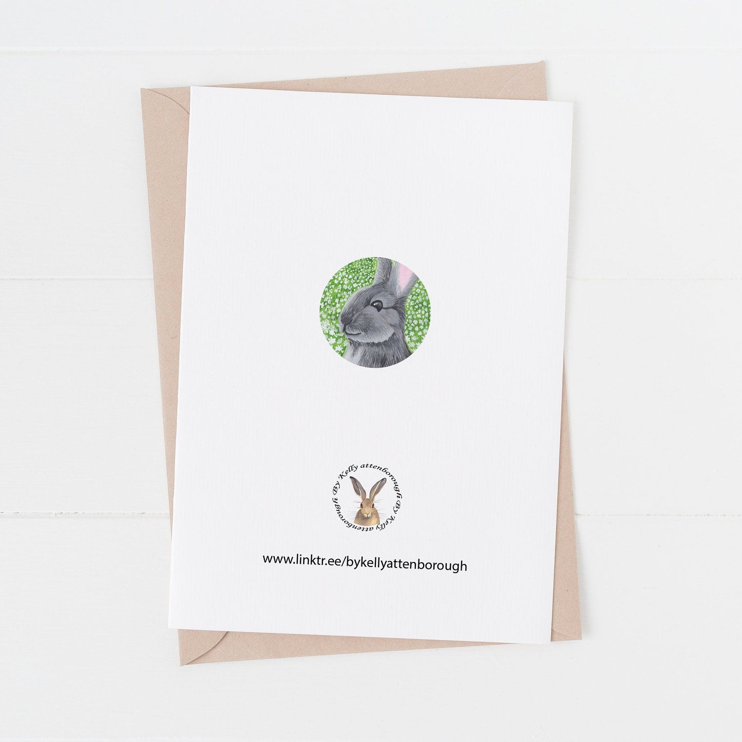 Daisy Meadow Rabbit Birthday Card showing the back of the acrd with the brand logo and a little circle illustration of a grey rabbit. Card laying on a white surface.