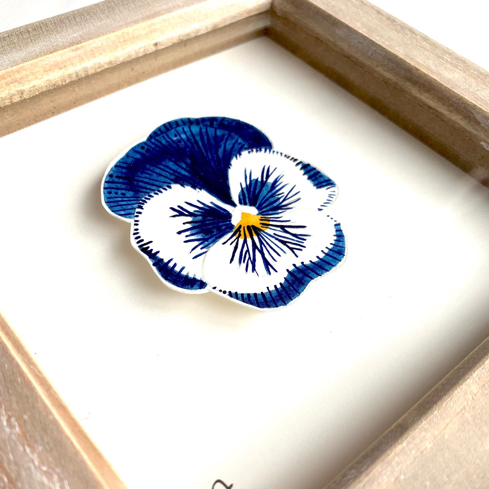 Framed artwork of a blue and white pansy flower with a signature on a white background