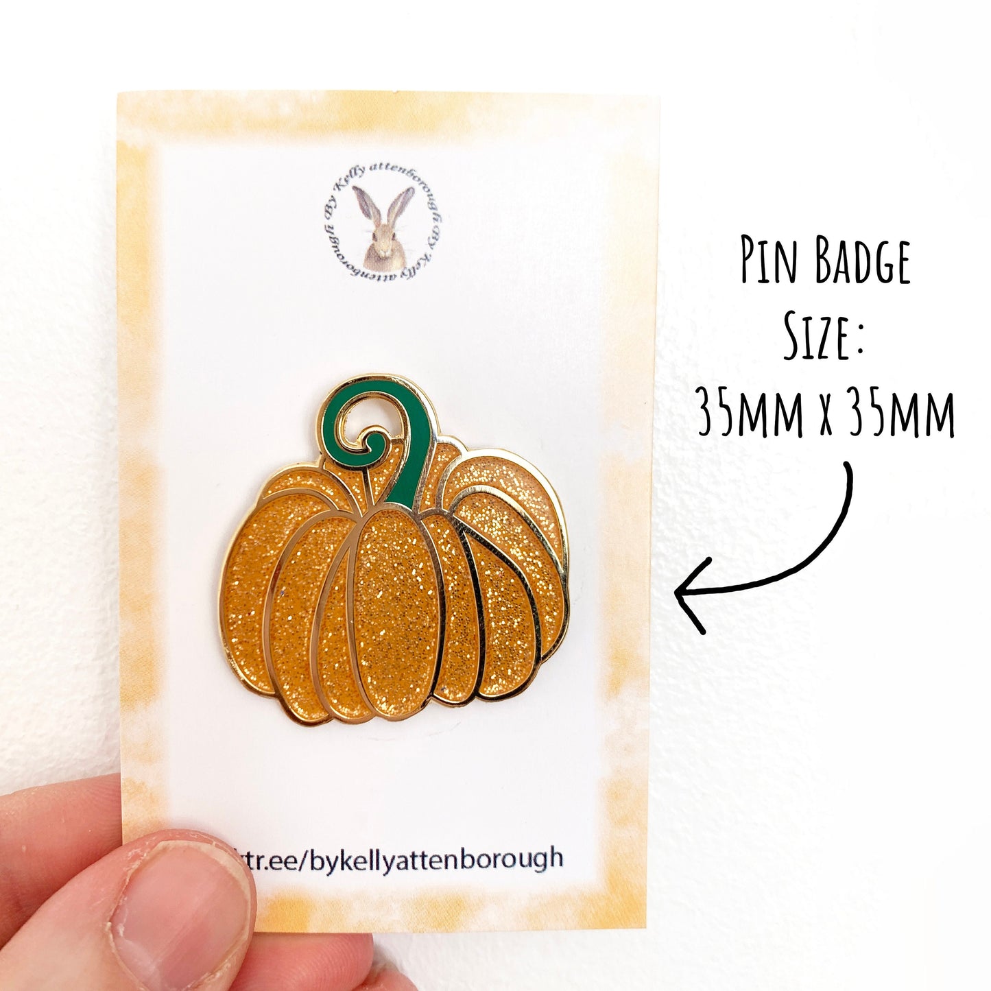 Fairytale Pumpkin Enamel Pin Badge on its backing card being held up against a white background with the text pin badge size: 35 x 35mm.