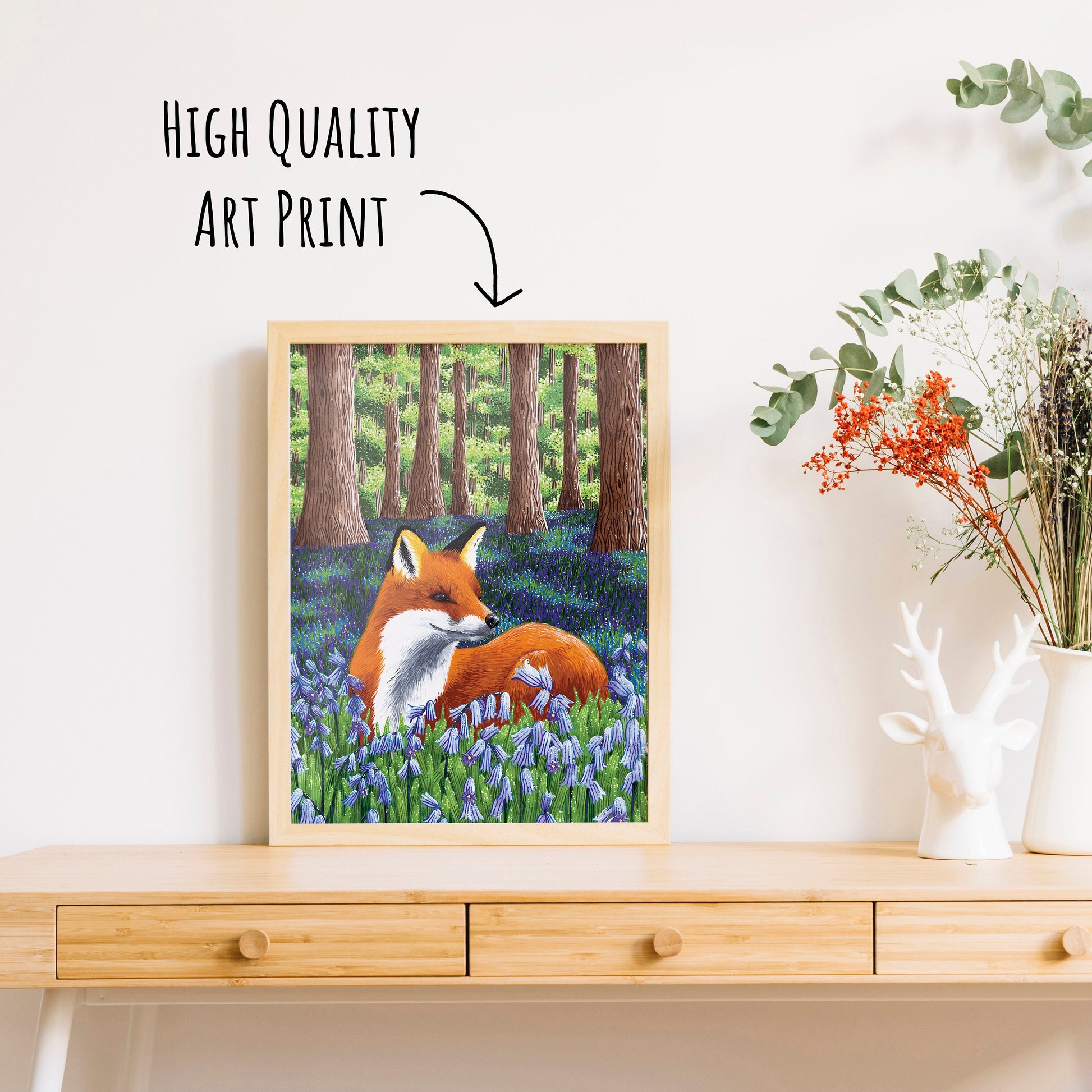 an art print of a fox laying amongst the bluebells in a woodland. placed in a wooden frame.