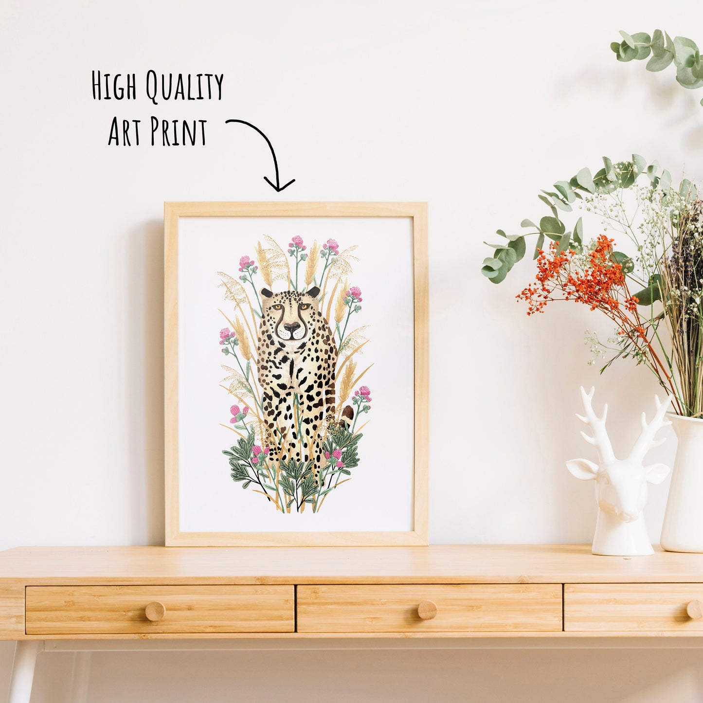 Golden Cheetah Art Print shown in a light wooden frame on a table top with a vase of dried foliage. (frame not included with purchase)