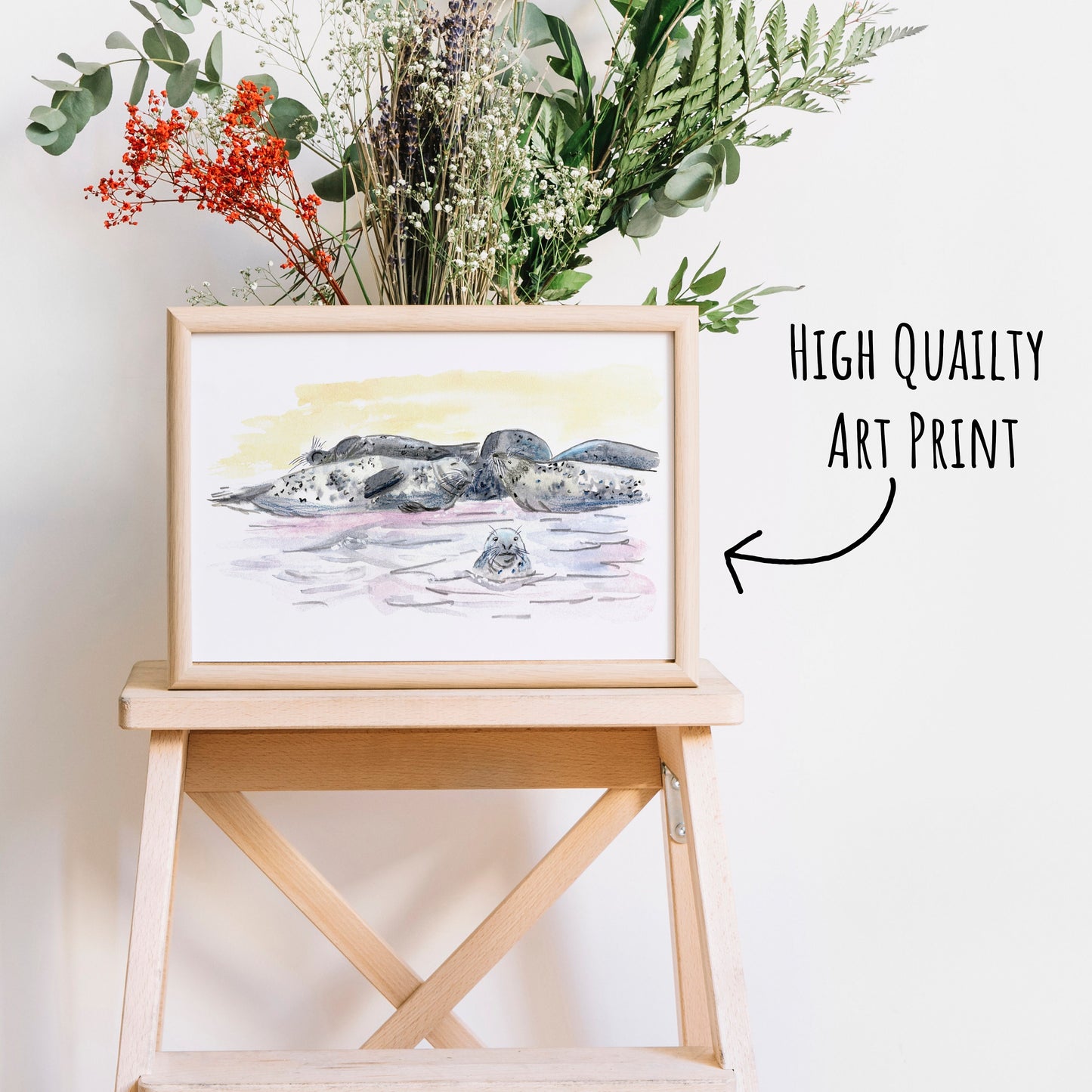 Grey Seal Art Print in a light wooden frame on a coffee table with dried foliage behind it.