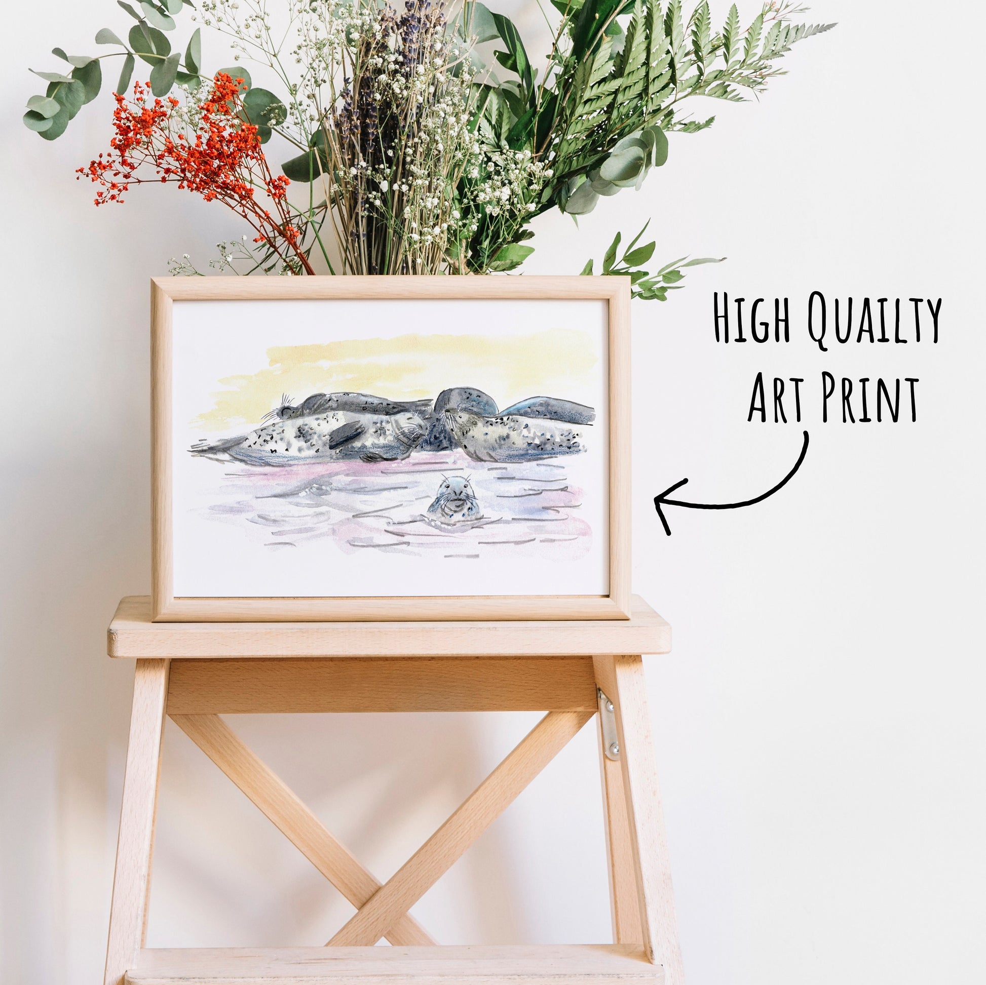 Grey Seal Art Print in a light wooden frame on a coffee table with dried foliage behind it.