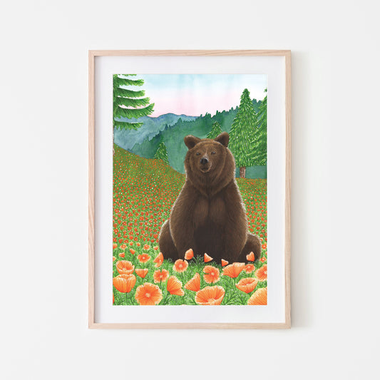 Art print of a brown grizzly bear sitting in a field with orange Californian poppies and mountainous hills in the background, framed in a light wooden frame. (framed not included in purchase)