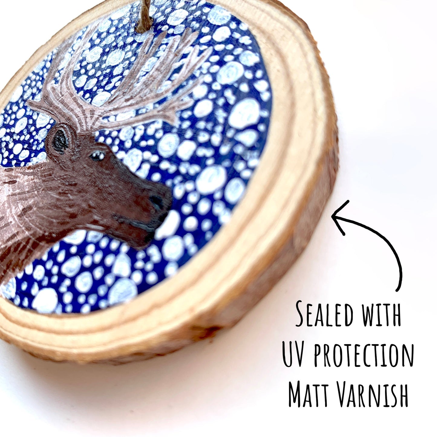 Hand Painted Reindeer Wood Slice Ornament close up showing the painted details of the illustration with the text: sealed with uv protection matt varnish.