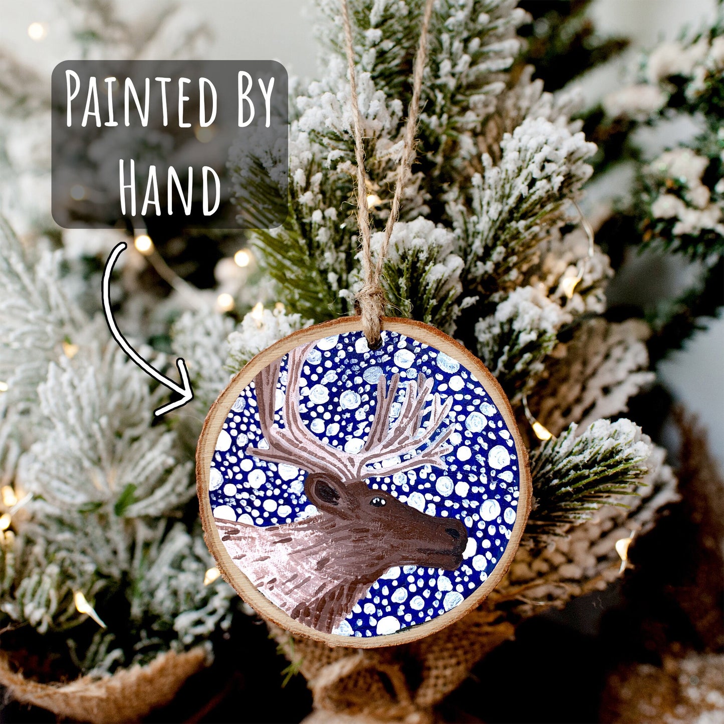 Hand Painted Reindeer Wood Slice Ornament hanging on a mini snowy christmas tree with the text painted by hand.