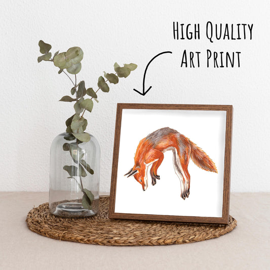 Jumping Red Fox Art Print framed in a dark wood frame on a straw placemat with a vase with a eucalyptus branch.