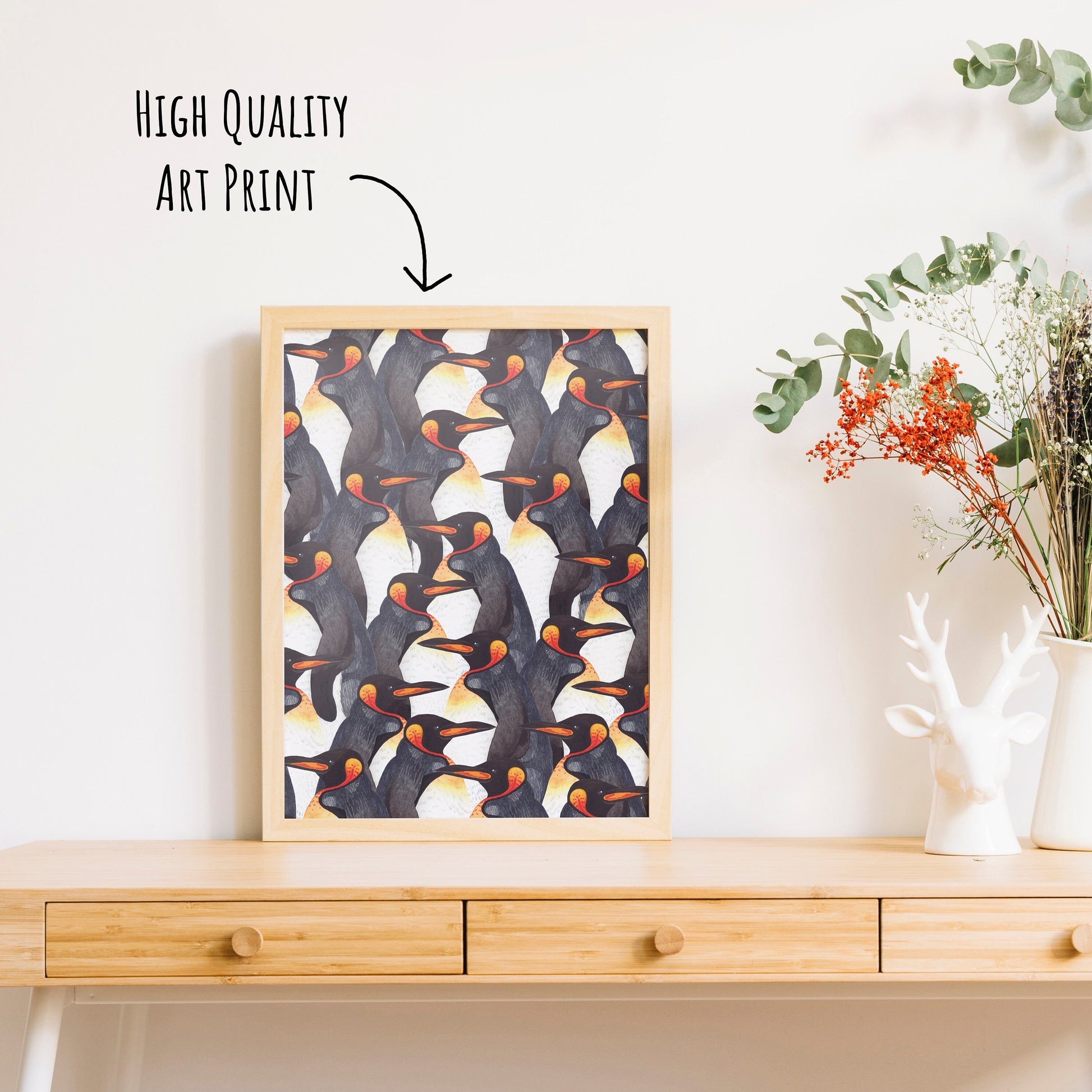King Penguin Pattern Art Print shown in a light wooden framed on a table top with a vase of dried foliage. 