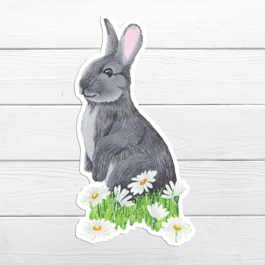 A sticker depicting a grey rabbit sitting on green grass with white daisies around its feet.