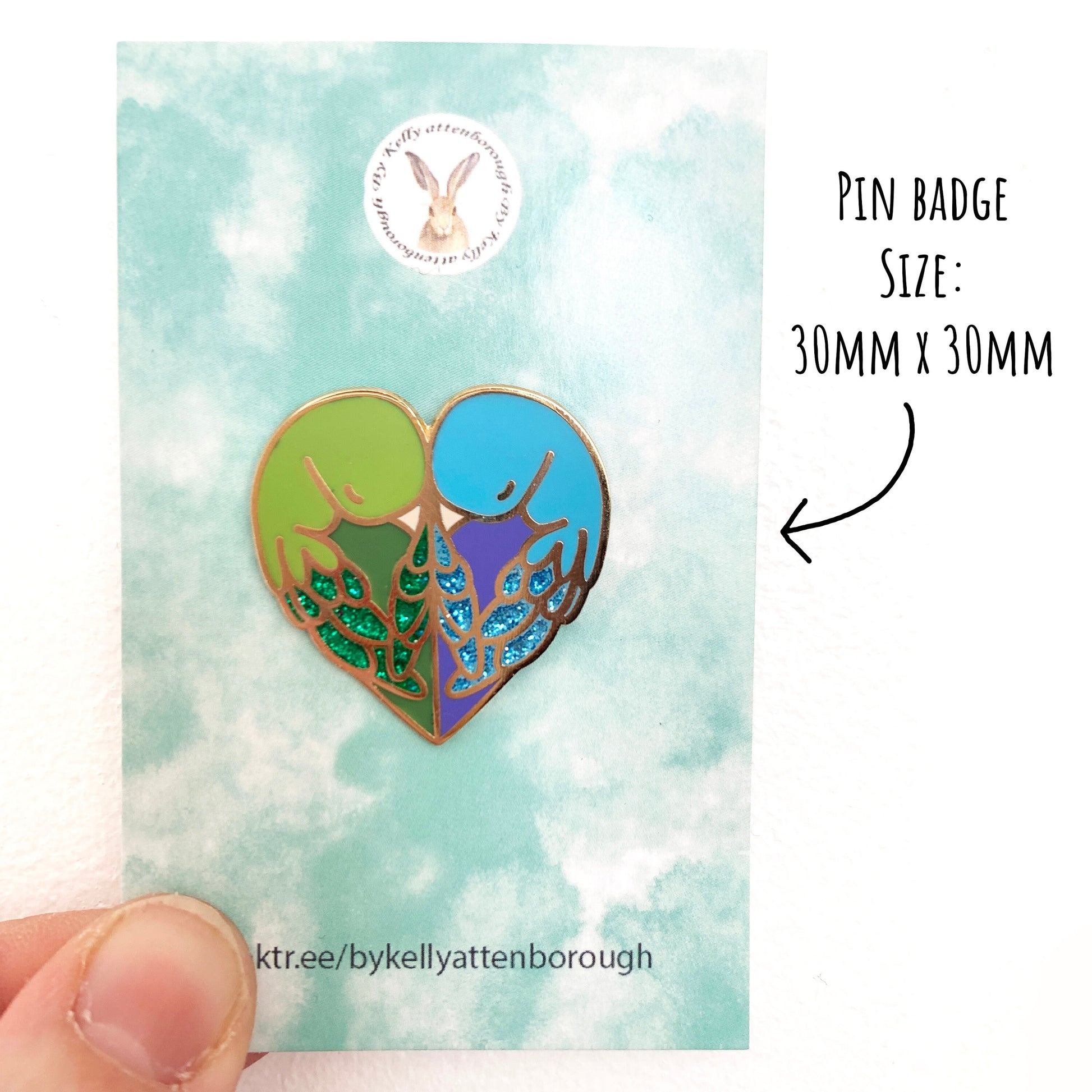 Love Birds Enamel Pin badge in its pale blue backing card being held up against a white background.With the text pin badge size: 30mm x 30mm.