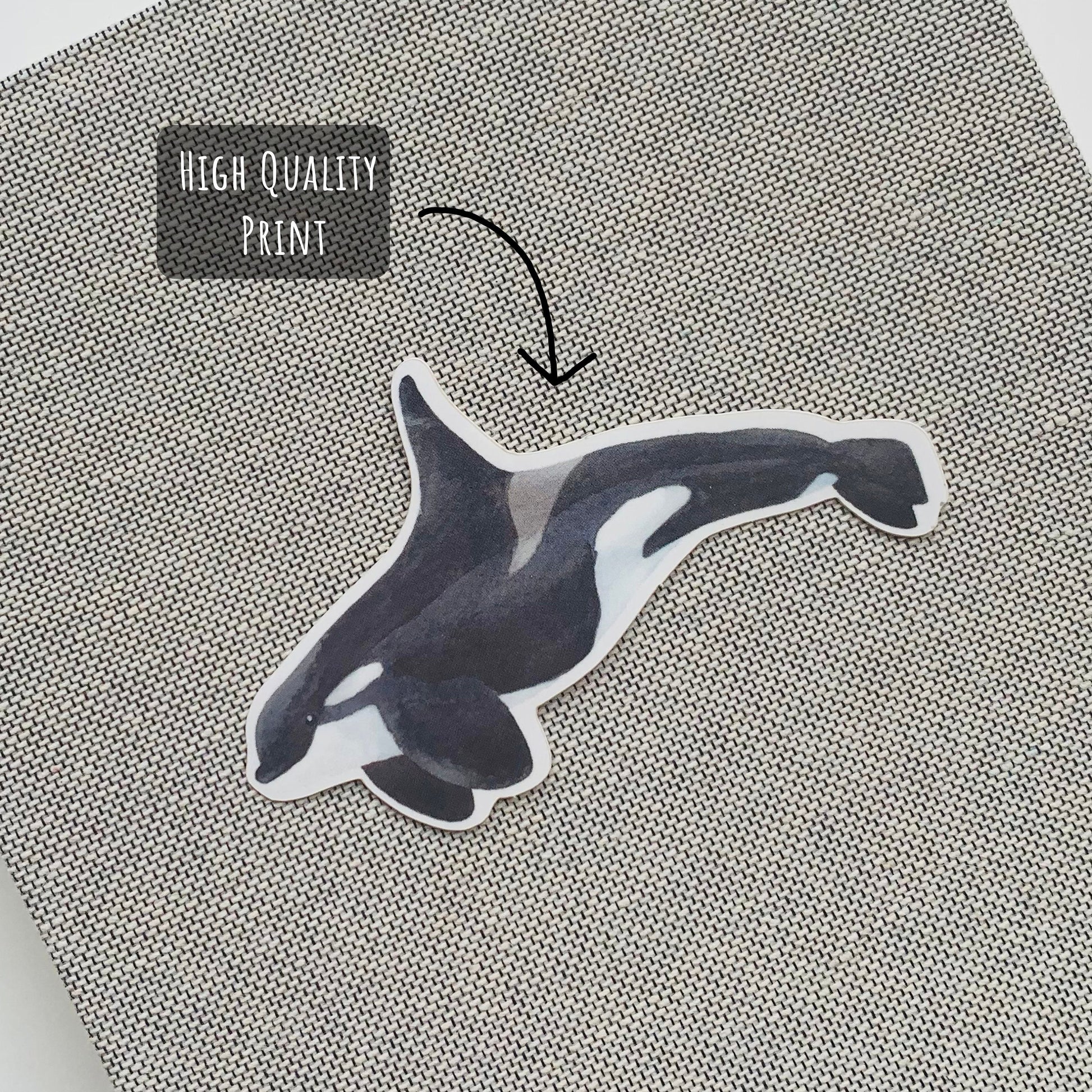 Orca Whale Sticker placed on the front on a grey notebook with the text high quality print.