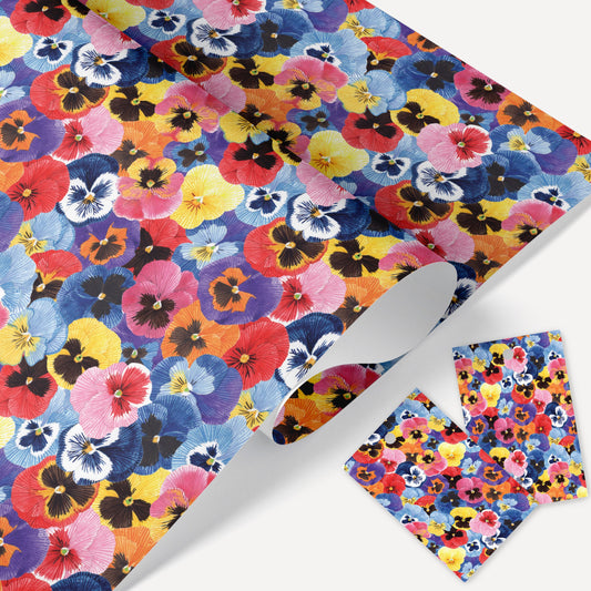 A sheet of wrapping paper with a vibrant, multicolored pansy flower pattern, displayed alongside two tags with the same design.