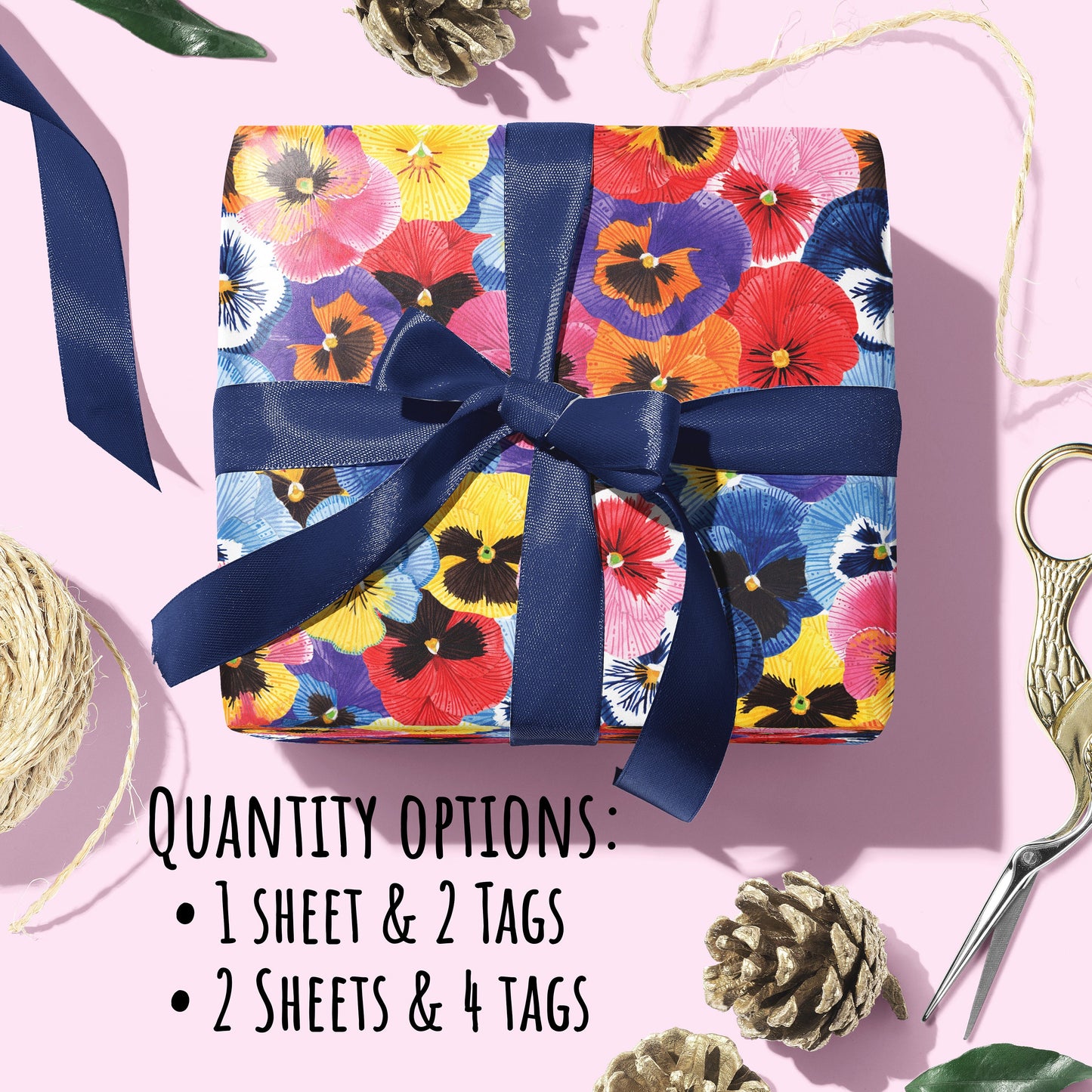 A present wrapped in the Pansy Flower Wrapping Paper with a dark blue silk ribbon bow place in a light pink surface. With the text Quantity options: 1 sheet & 2 tags, 2 sheets & 4 tags.