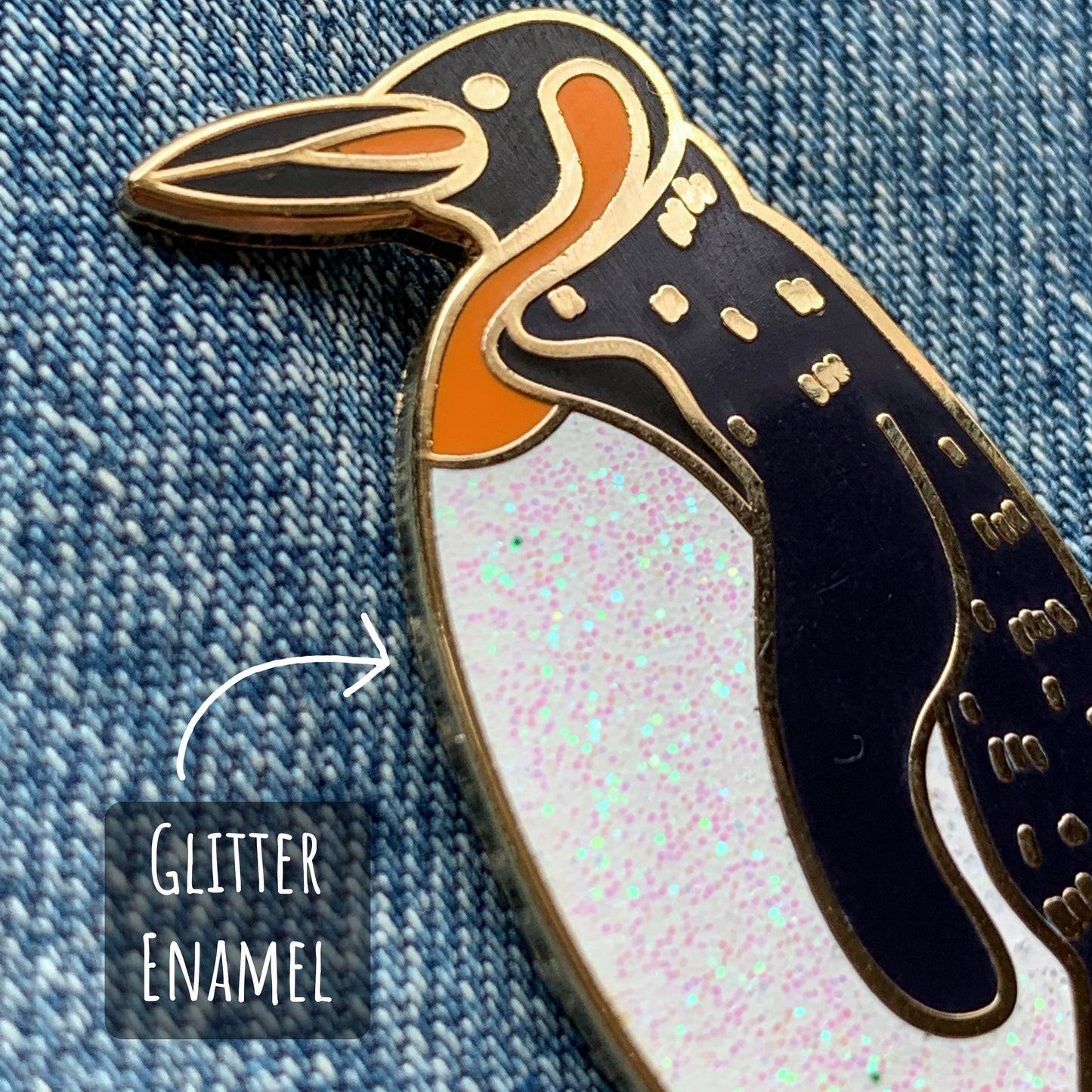 Penguin Enamel Pin Badge close up showing the details and textures on the pin badge, with the text glitter enamel.