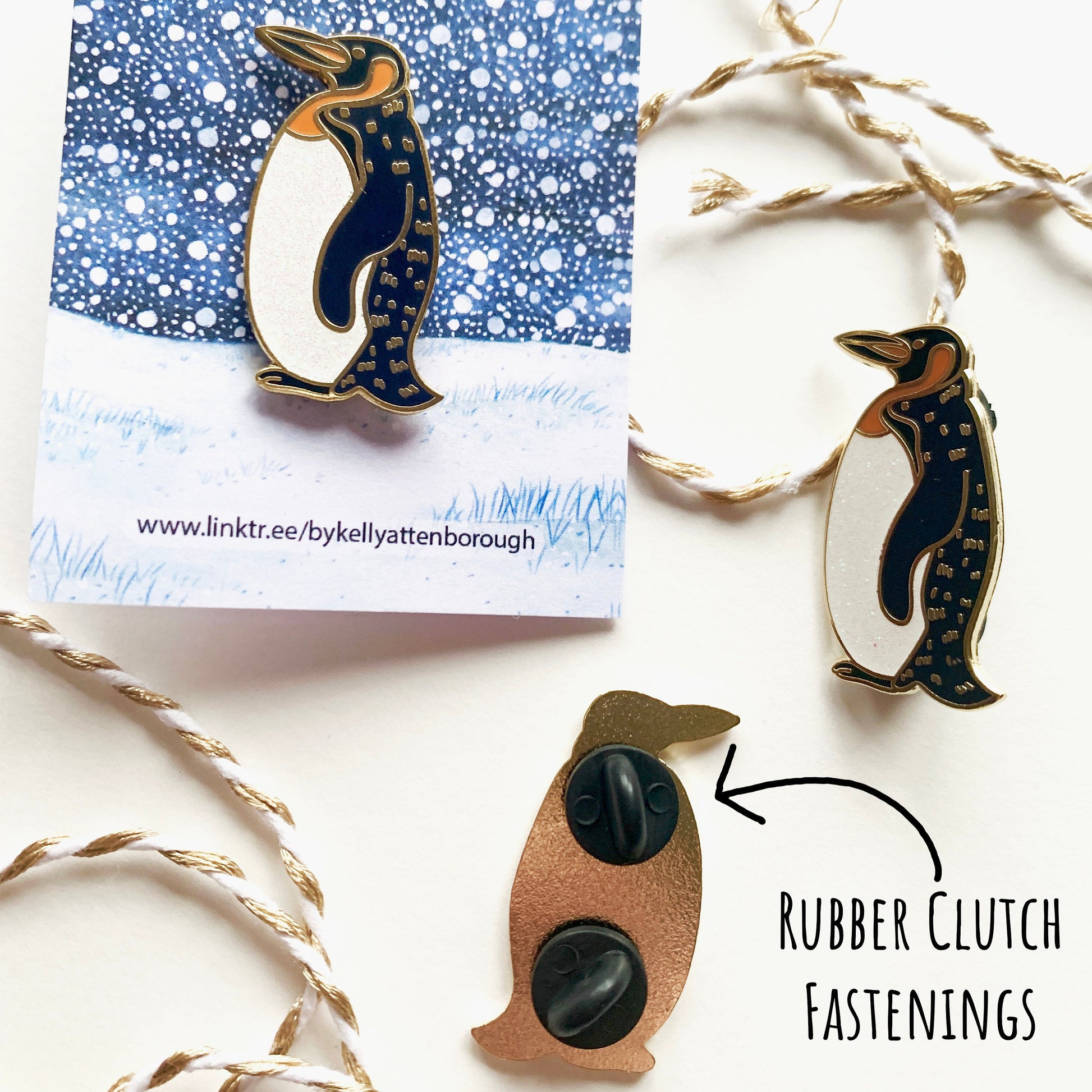 Showing three on the Penguin Enamel Pin Badges. One on its backing card, another without and the third one showing the back with its two black rubber clutch fastenings. All place on a white surface with the text rubber clutch fastenings.