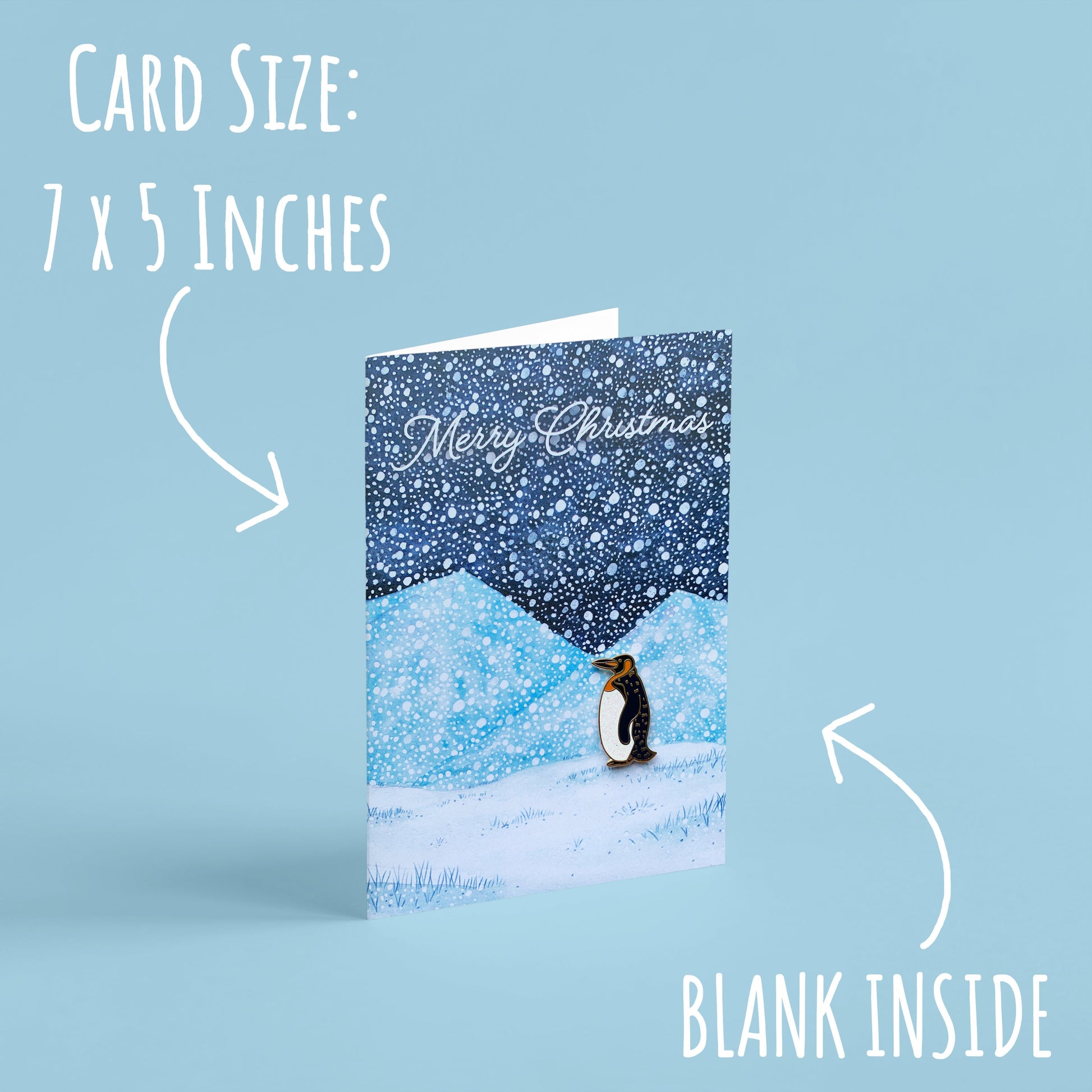 Penguin Enamel Pin with Christmas Card standing with a light blue backgournd with the font card size: 7 x 5 inches and blank inside.