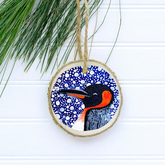 A hand-painted wooden Christmas ornament featuring a winter penguin with a jute twine string for hanging.