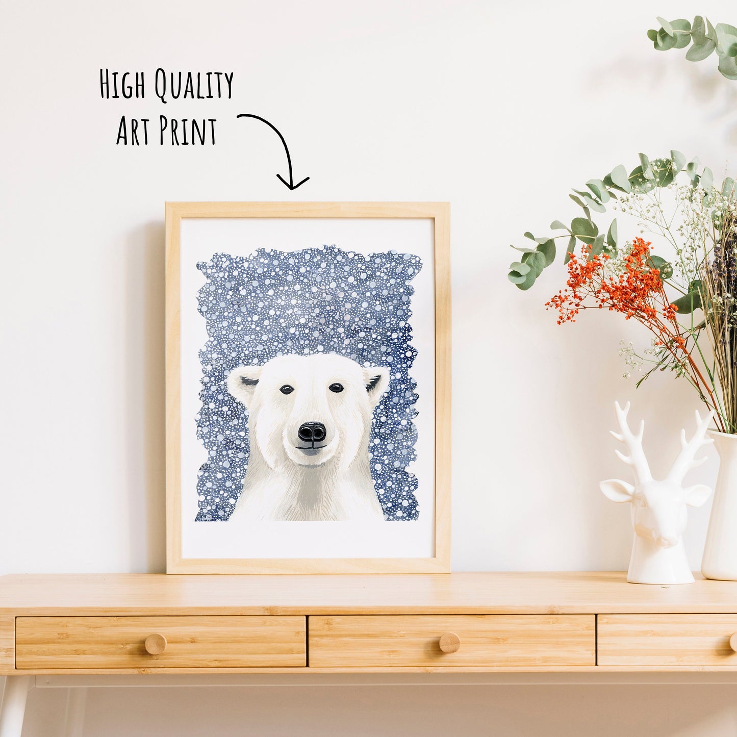 Polar Bear Art Print shown in a light wooden frame on a table top next to  a vase of dried foliage. (frame not included with purchase)