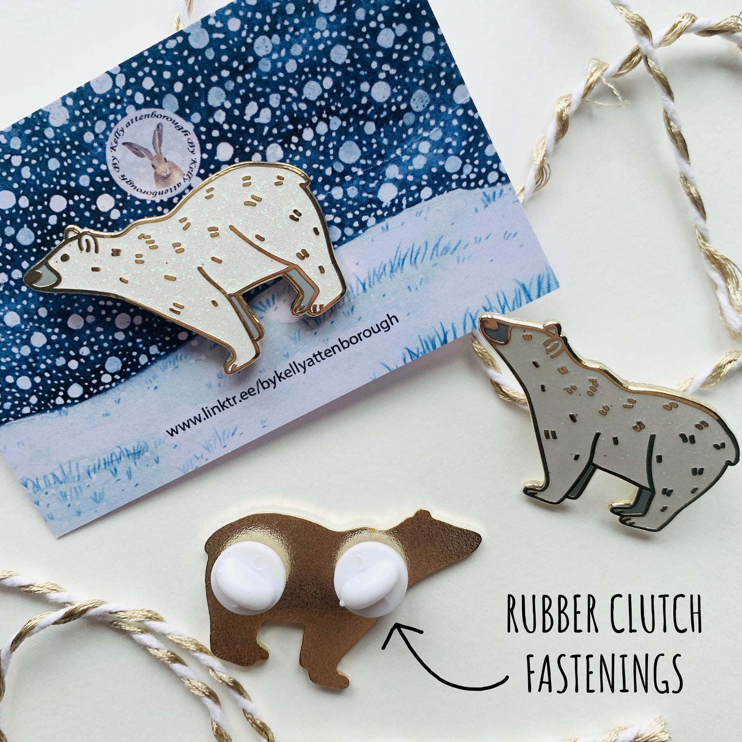 showing three of the Polar Bear Enamel Pin Badges. One with its backing card, one with out and the third one showing the back with the two white rubber clutch fastenings. All on a white surface with the text rubber clutch fastenings.