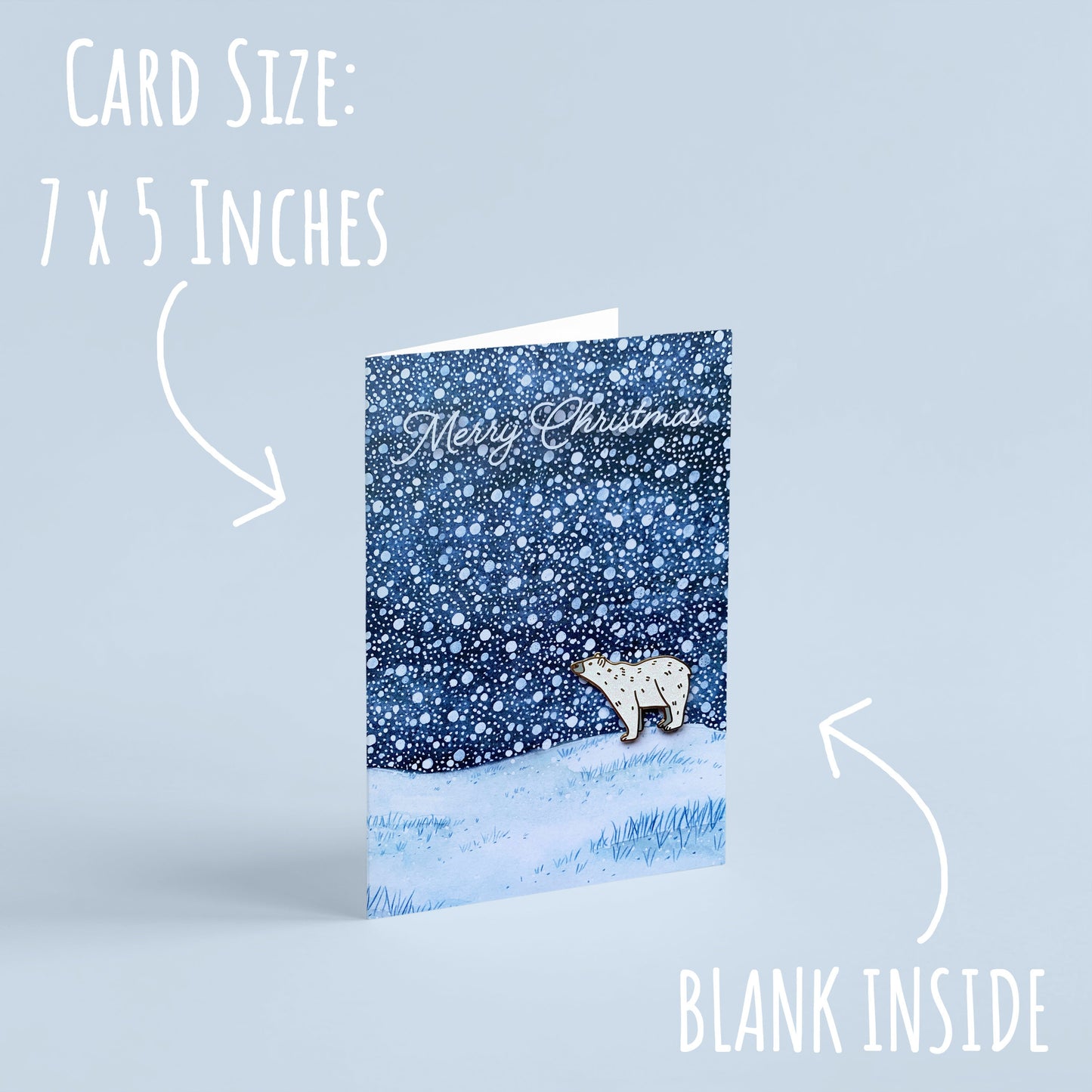 The Polar Bear Pin Badge Christmas Card standing with a pale blue background with the text card size: 7 x 5 inches & blank inside.