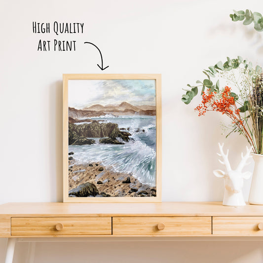 The Portstewart Art Print in a light wooden frame on a table top next to a vase of dried foliage.
