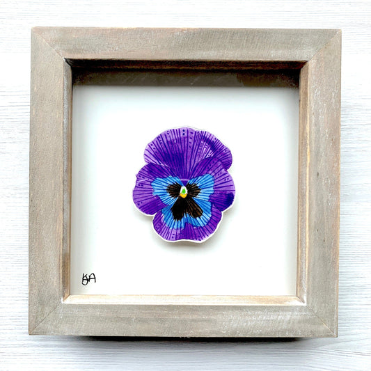 A hand-painted watercolor painting of a purple blue & black pansy flower, framed in a rustic washed effect frame.