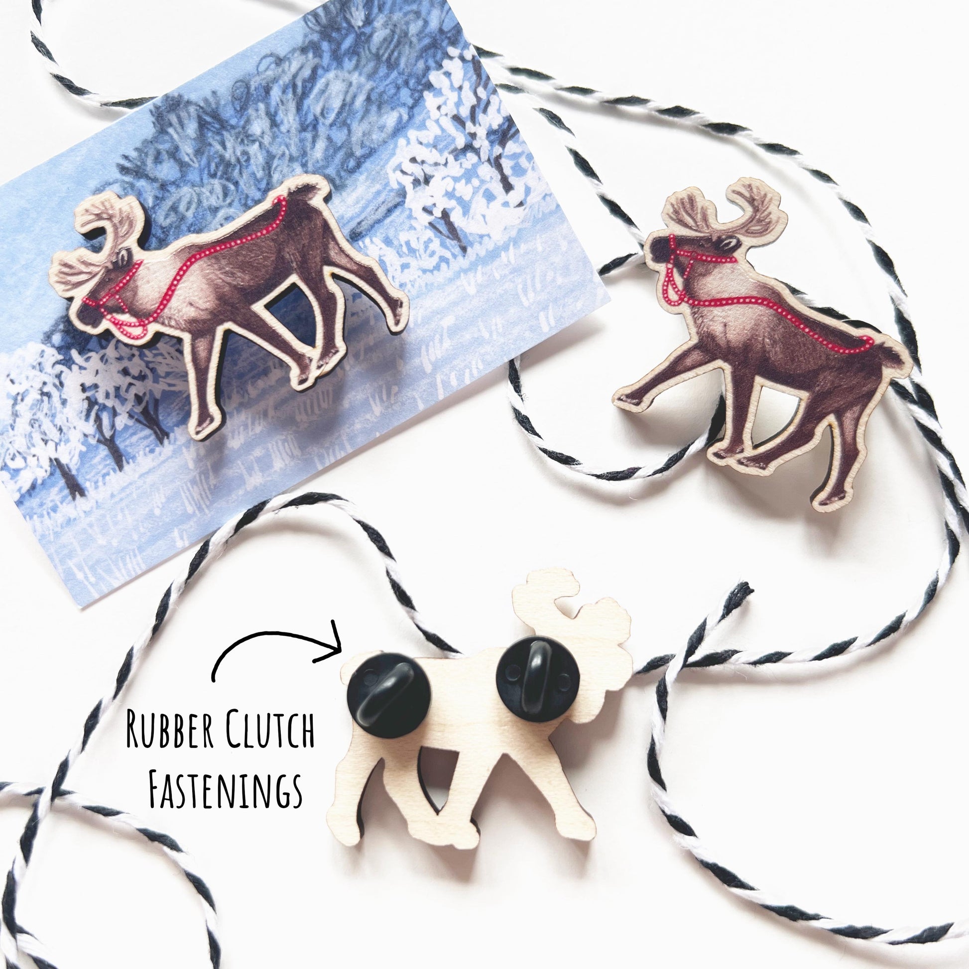 showing 3 of the Reindeer Maple Wood Pin Badges. One and its backing card one without and the third one showing the back with two rubber clutch fastenings. Placed on a white surface with the text rubber clutch fastenings.