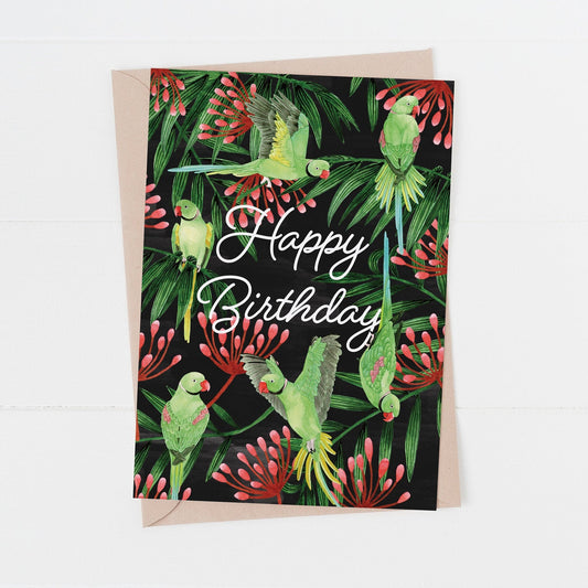 A birthday card with an illustration of green ring-necked parakeets among tropical flowers, with 'Happy Birthday' text at the top.