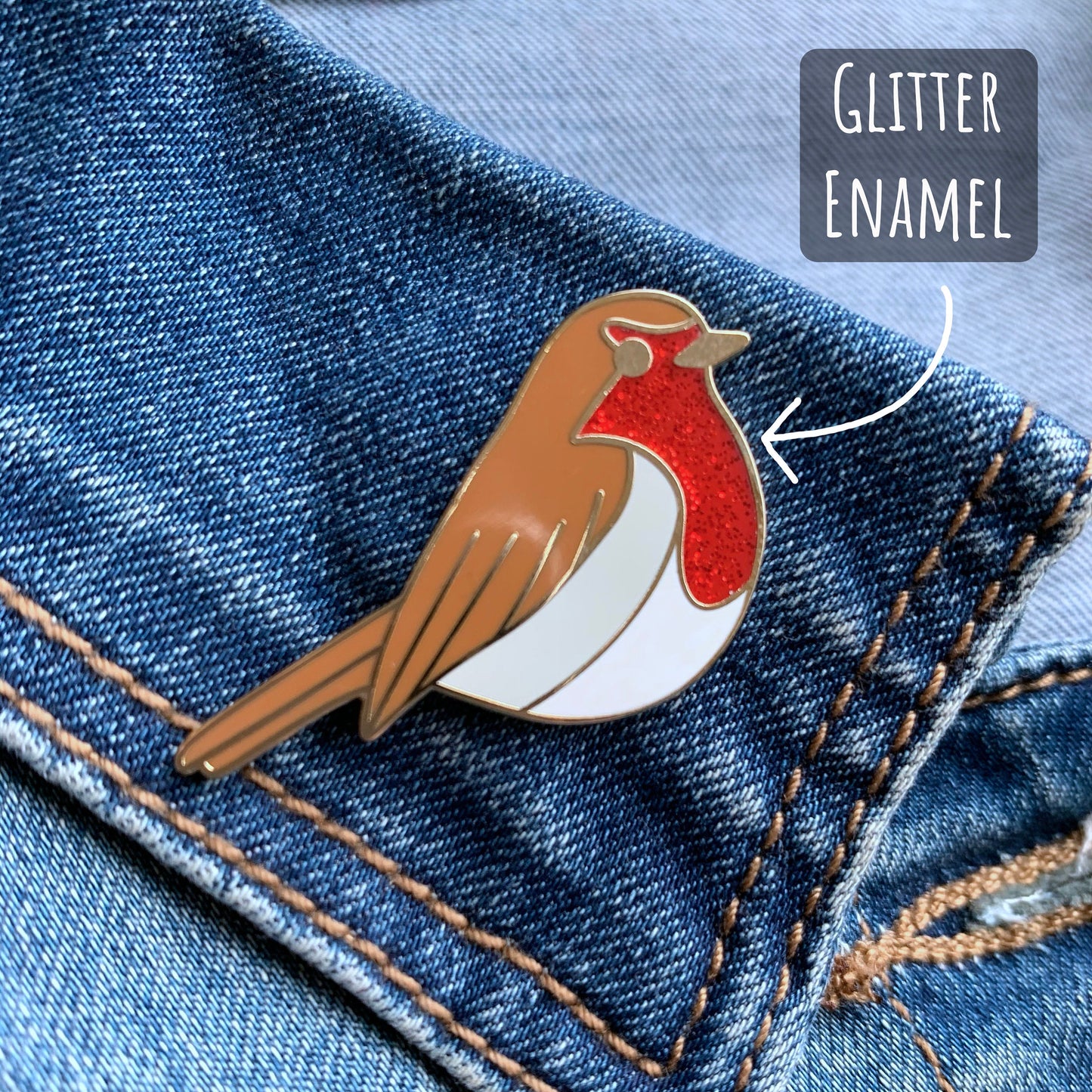 Robin Enamel Pin Badge close up showing the details of the red glitter, brown and white enamels of the pin badge. with the text Glitter enamel.